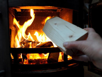 Eine Frau heizt einen Holzkamin ein. Foto: Angelika Warmuth/Archiv