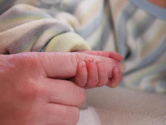 Ein Finger der Hebamme wird von der Hand des Neugeborenen gehalten. Foto: Uli Deck/Archiv