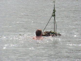 Das von den Kindern gebaute Floß wird von einem wagemutigen Schwimmer weit in die Strömung des Rheines hinausgebracht.