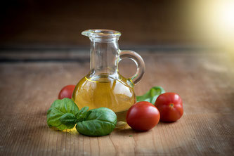Ein Krug Olivenöl neben Gemüse