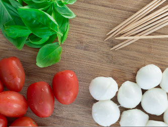 Mozarella, Tomaten, Basilikum und Stäbchen auf einem Teller. 