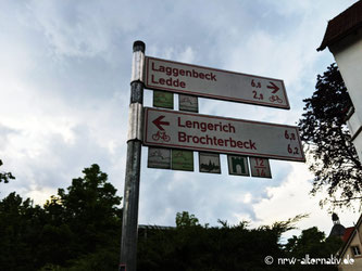 Ein rotes Fahrrad-Wegeschild, im Hintergrund Bäume.