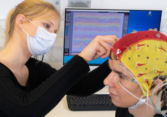 (C) Doktorandin Celina von Eiff befestigt Elektroden an einer Kappe, die der Proband Lucas Riedel während einer EEG-Studie mit Cochlea-Implantaten an der Universität Jena trägt. Foto: Jens Meyer/Uni Jena