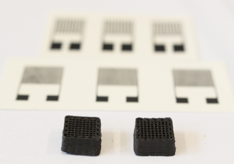 Neuartiger Werkstoff für gedruckte Schaltungen: Zwei Testquader von einem Zentimeter Breite aus dem 3D-Drucker. Im Hintergrund sieht man die gedruckten elektronischen Sensoren. Bild: Empa