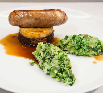 Gebratene Wurst auf einem Türmchen aus Lebkuchentaler und Apfelring mit einem Saucenspiegel und zwei Nockerl Rahmwirsing