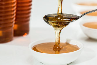 Honig fließt über einen Löffel in eine Schale. Honigmassage bietet eine sanfte Anwendung und fördert tiefe Entspannung.