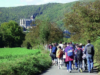 Cette image représente des élèves en randonnée vers la cité médiévale de Saint-Bertrand-de-Comminges, vue du côté de la basilique Saint-Just de Valcabrère.