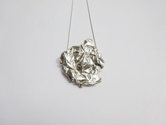 Un très gros pendentif au design froissé est placé sur une chaine fine en argent.