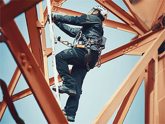 Arbeiter mit Helm und Auffang-und Haltegurte an einer Leiter gesichert durch ein mitlaufendes Auffanggerät