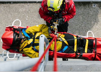 2 Personen (eine Person liegt in einer Rettungstrage) werden abgeseilt.