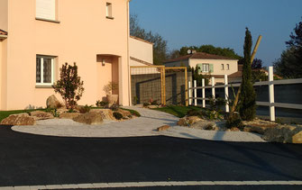 C'est une photo du jardin avec un enrobé noire, pavage béton une clôture bois , une rocaille en granit dans les massifs d'arbustes, arbres et vivaces à saint julien de concelles, le landreau, loroux bottereau, vertou, basse goulaine