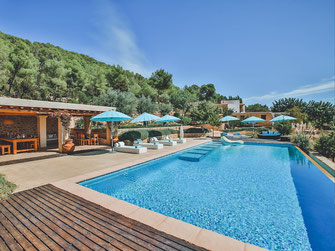 Swiming pool in Ibiza, blue sky and pine trees with a cozy brown, wooden Bali bed