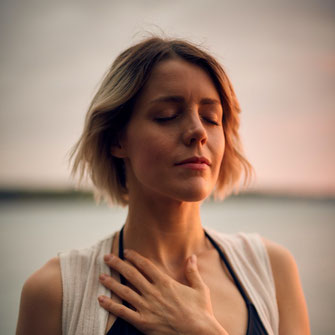 Frau mit geschlossenen Augen, Meditation, Stille, Frieden, ganz bei sich, eine Hand auf dem Herzbereich