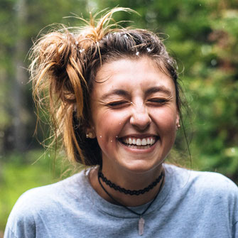 junge Frau mit vor Lachen zusammengekniffenen Augen, Haare lässig hochgesteckt, Spritzer von Wasser im Gesicht