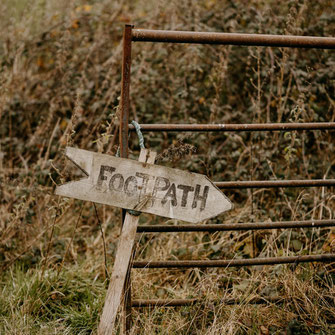 hölzerner Wegweiser mit der Aufschrift "Footpath" an Weidezaun befestigt