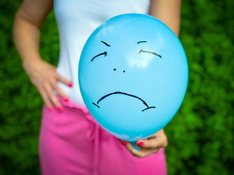 Eine Frau halt sich einen aufgeblasenen Luftballon mit Grummel-Gesicht vor den Bauch