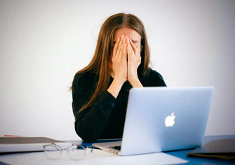 Erschöpfte Frau schlägt vor dem Laptop die Hände vor dem Gesicht zusammen