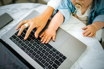 Frau bespaßt Baby auf dem Schoß und arbeitet zugleich am Laptop 