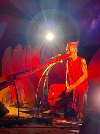 Ansgar Stein on stage in Forlimpopoli. Dressed in red, playing red didgeridoos, sitting on a cajon.