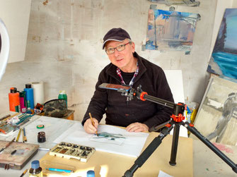 Ich sitze im Atelier am Arbeitstisch und male für ein Video