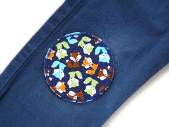 ein runder Hosenflicken mit vielen kleinen Füchsen ist auf eine dunkelblaue Hose als Flicken aufgebügelt