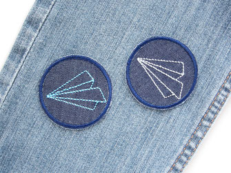 !B auf eine blaue Jeanshose wurden als kleine Flicken zwei Aufbügler mit aufgesticktem Papierflieger aufgebügelt
