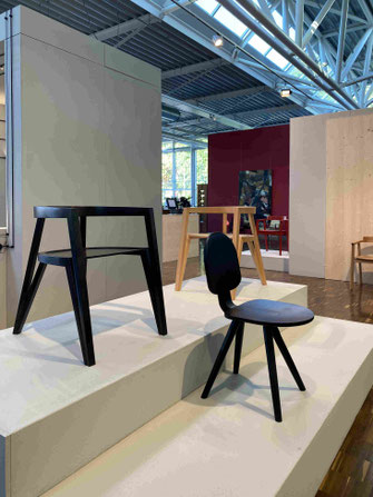Zwei dunkle und ein heller Designerstuhl auf einem Ausstellungspodest im Planungsbüro der Deutschen Werkstätten