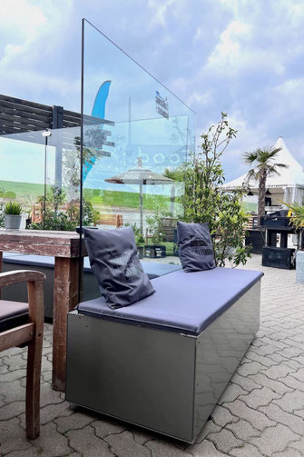 Sitzbank-Modul mit integriertem Glas-Windschutz und grauen Polstern in einer entspannten Strandbar-Atmosphäre, ideal als komfortable Sitzgelegenheit im Außenbereich