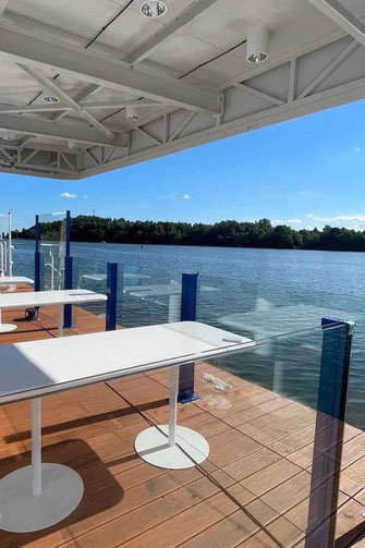 Höhenverstellbare Glas-Balustrade mit blauem Rahmen als transparenter Windschutz an einem Holzsteg am Wasser