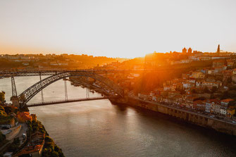 Eine Drohnenaufnahme zeigt den malerischen Sonnenuntergang über den Dächern von Porto mit der bekannten Brücke Ponte Dom Luis.