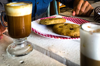 Two coffees on white table with plate and cookies.