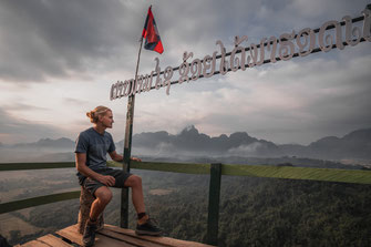 Un homme est assis sur une plate-forme d'observation et regarde Vang Vieng en contrebas.