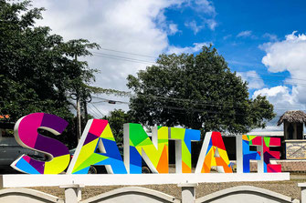 Colorful lettering with the name of the city of Santa Fé with green trees in the background.