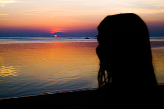 Frau bewundert farbenprächtigen Sonnenuntergang auf Koh Phangan.
