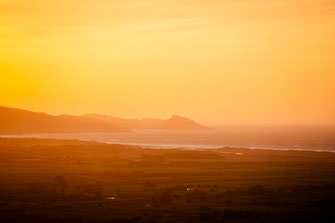 Die Umrisse der entfernten Stadt Castelsardo am Horizont bei untergehender Sonnne.