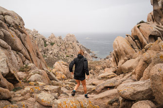 Eine Frau steigt über große Felsen hinab ans Meer.