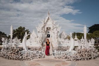 Eine Frau mit einer langen roten Hose schreitet über die Brücke des weißen Tempels in Chiang Rai.