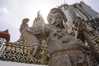 A stone war stands in the foreground of Wat Arun in Bangkok.