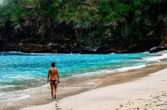 Frau spaziert alleine am Strand vom Pandan Beach entlang.