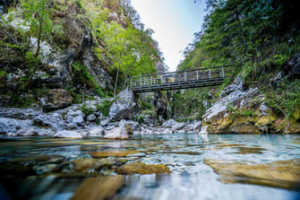 Langzeitbelichtung des Flusses der Tolmin Klamm und der Holzbrücke, die sich über die Felsen spannt.