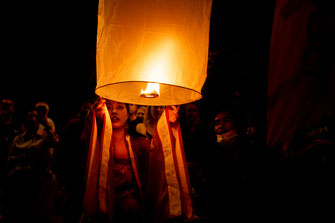 A woman in traditional costume raises a lighted sky lantern in Chiang Mai.