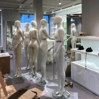 Genesis Schaufensterpuppen, 6 Mannequins stehen in einem sich im umbau befindlichen Kleidergeschäft. Leere Regale und Stangen und Verpackungsmaterial ist zu sehen.
