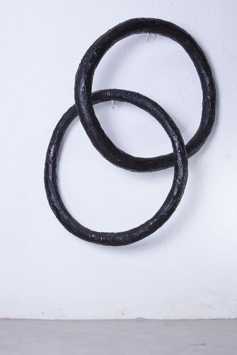 hello sorry ist eine Wandinstallation von Oliver Braig. Zu sehen sind zwei große schwarze Ringe, die ineinander verbunden sind. Wie zwei Glieder einer Kette. Oder wie das Symbol für Ehe. Die Holzringe sind mit einer dicken Schicht Epoxidharz überzogen.  
