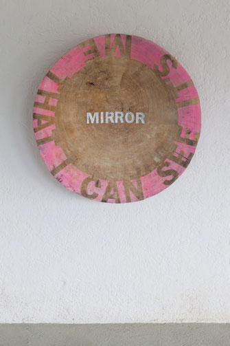 Mirror, it's me that I can see. Eine Baumscheibe an der Wand. In der Mitte der Scheibe steht das Wort MIRROR. Oliver Braig stellt Fragen. Was sehe ich, wenn ich in den Spiegel schaue? Was kann ich sehen, wenn ich vor einem Spiegel stehe? Sehe ich das, was