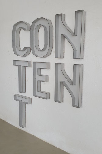 Die Wandinstallation CONTENT mit dem Titel WITHOUT CONTENT von Oliver Braig ist aus weißen Kartonbuchstaben gefertigt. Die Kartonränder sehen aus, als wären sie gezeichnet. Black Friday? Inhalt.