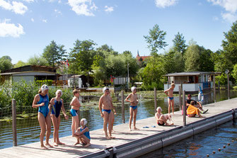 Junge Schwimmer und Schwimmerinnen, die während eines Sommerferien-Camps des WSW Rostock auf einem Schwimmsteg im Flussbad Rostock stehen