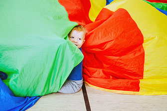 Ein Kind spielt beim Eltern-Kind-Turnen mit einem bunten Tuch