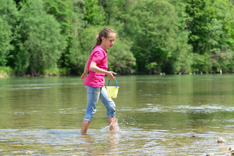 Ein Mädchen läuft mit einem kleinen Eimer in der Hand durch ein flaches Gewässer