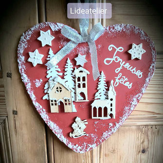 suspension coeur en MDF d'envrion 20 cms peint couleur rouge avec décors en bois représentant des maisons ruban argenté écriture Joyeuses fêtes