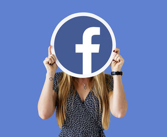 junge Frau hält sich facebook-logo vor das gesicht